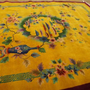 Saturated yellow rug with a colorful floral and vase pattern, maroon edge, and geometric green border on wood.