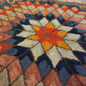 Close-up of a high-pile, hooked rug featuring a central orange star surrounded by multicolored diamond shapes.