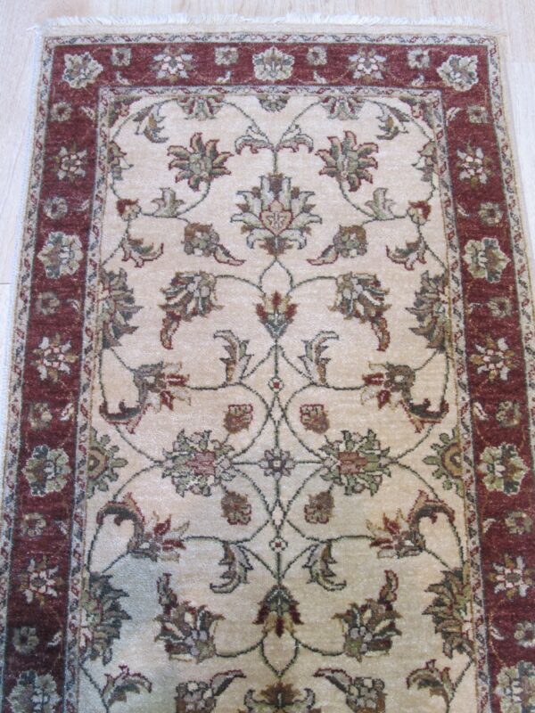 A small traditional rug displays intricate green and red floral patterns on a light tan ground.