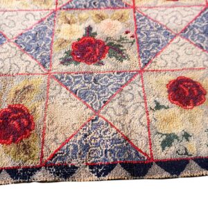 Textured rug close-up showing a geometric patchwork design with red roses, blue patterns, and a navy triangular border.