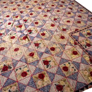 Beige, blue, and red floral rug featuring a diamond geometric pattern with repeating red rose motifs.