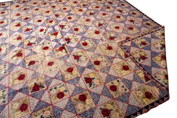 Beige, blue, and red floral rug featuring a diamond geometric pattern with repeating red rose motifs.