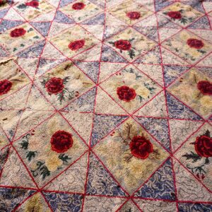 Textured rug with repeating diamond pattern outlined in red, featuring dark red roses and blue segments.