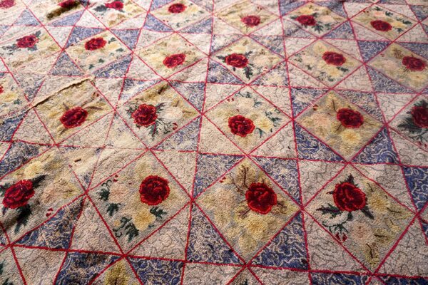 Textured rug with repeating diamond pattern outlined in red, featuring dark red roses and blue segments.