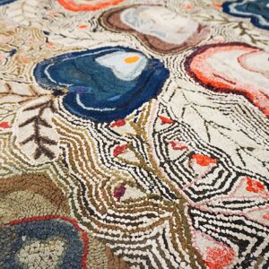 Closeup of a textured rug featuring abstract blue, coral, and brown shapes with wavy black and cream lines.