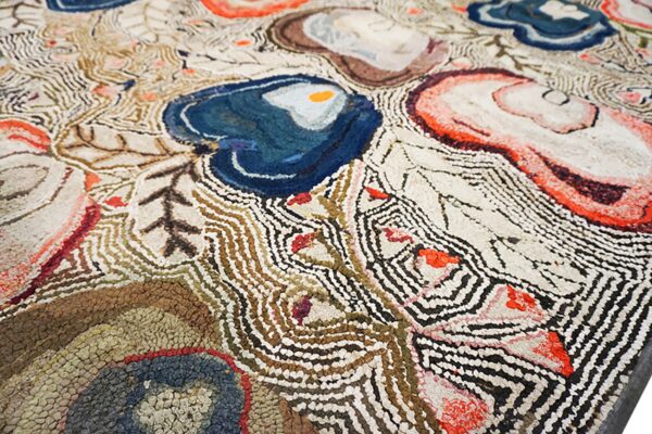Closeup of a textured rug featuring abstract blue, coral, and brown shapes with wavy black and cream lines.