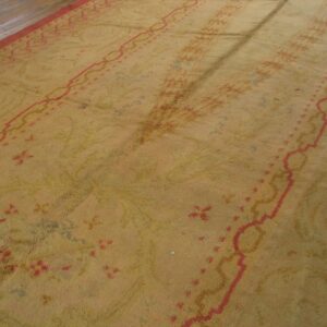 High-pile gold rug with faded coral and blue patterns sits adjacent to dark wood planks.