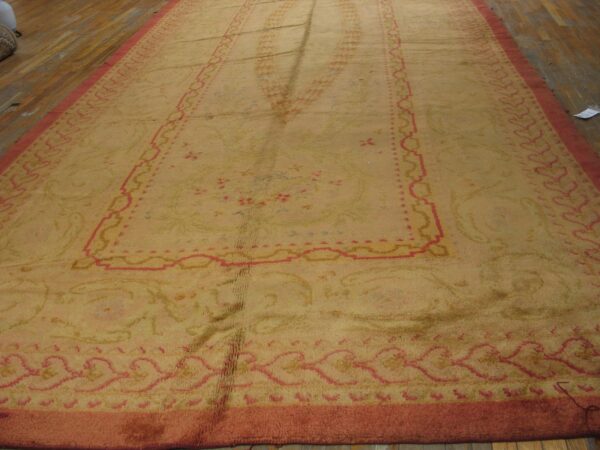 High-pile gold rug with large traditional pink borders spread across worn wooden plank flooring.