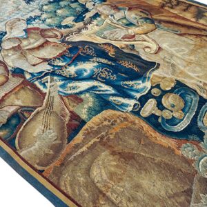 Detail of a tapestry-style rug showing figures and foliage woven in deep blue, beige, and warm brown colors.