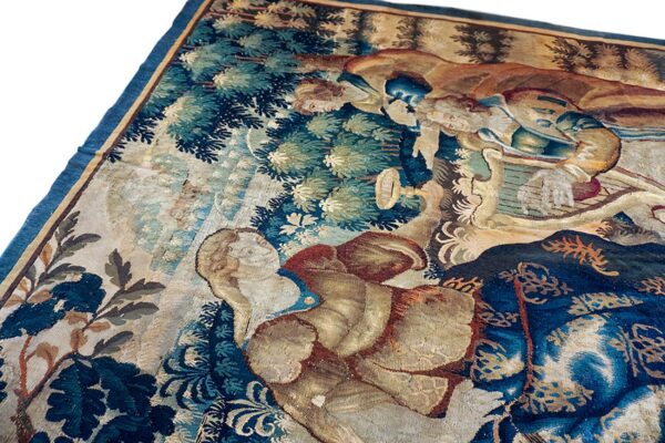Close-up of a flat-woven tapestry rug depicting figures and foliage in deep blue, tan, and muted green.