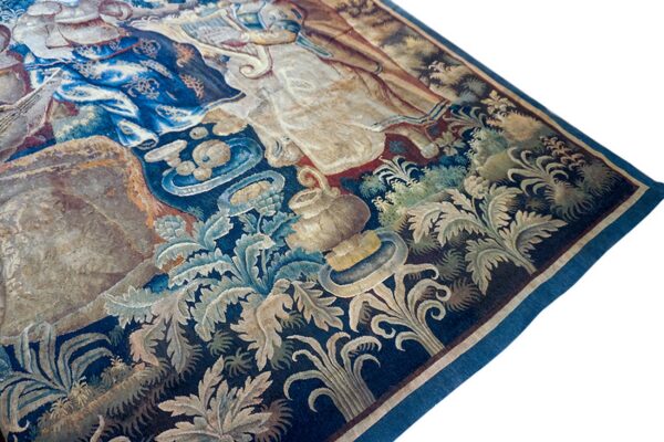 Detailed tapestry featuring figures and botanical motifs in deep blue, cream, and tan on a white background.