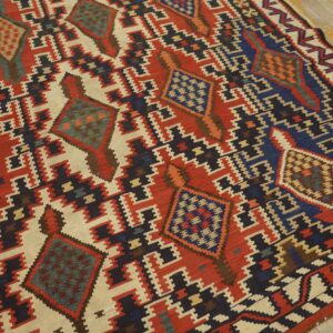 Flat-weave rug featuring a geometric pattern in red, cream, navy blue, and teal on distressed wood floors.