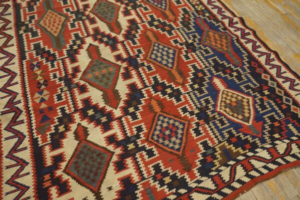 Flat-weave rug featuring a geometric pattern in red, cream, navy blue, and teal on distressed wood floors.