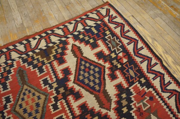 Geometric flatweave rug featuring stepped patterns in red, navy, and cream lying on rustic wood planks.