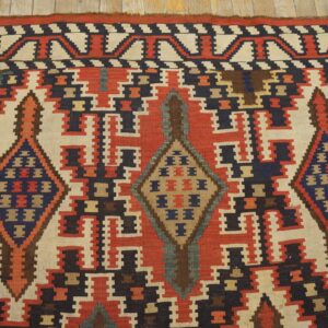 Flatweave rug with repeating geometric medallions in red, cream, navy, and brown on light wooden planks.