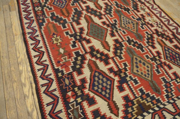 Geometric flat-weave rug in rust, ivory, and navy featuring bold stepped diamond patterns on wood flooring.