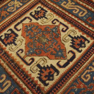 Low-pile geometric rug detail showing complex motifs in navy blue, rust, and beige on wood flooring.