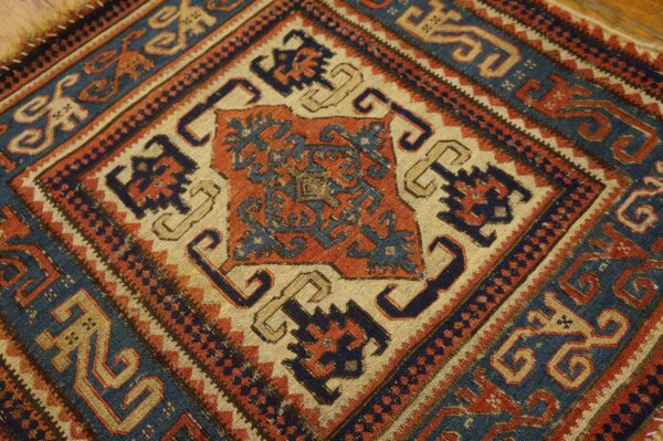 Low-pile geometric rug detail showing complex motifs in navy blue, rust, and beige on wood flooring.