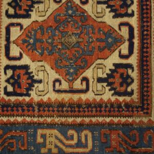 Geometric diamond pattern in navy and rust red on a cream field, bordered by zig-zags.