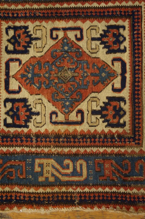 Geometric diamond pattern in navy and rust red on a cream field, bordered by zig-zags.