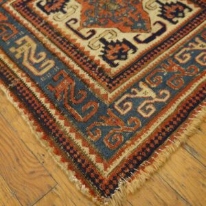 Low-pile rug corner showing blue, orange, and cream geometric borders on worn hardwood flooring.