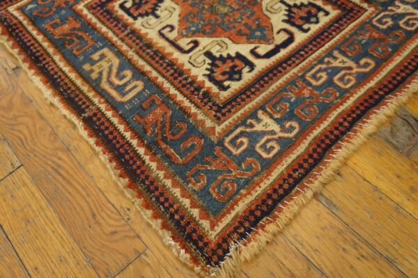 Low-pile rug corner showing blue, orange, and cream geometric borders on worn hardwood flooring.
