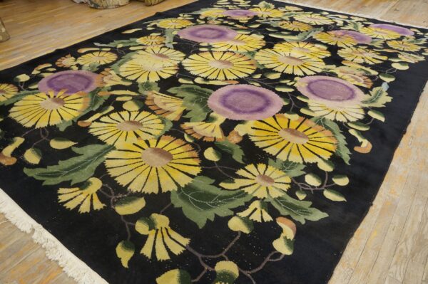 Black field rug with large yellow and purple stylized flowers, green leaves, and white fringe on wood floors.