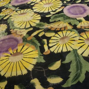 Stylized floral rug with yellow and purple flowers on black pile, resting on light wood flooring.