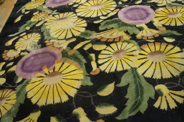 Stylized floral rug with yellow and purple flowers on black pile, resting on light wood flooring.