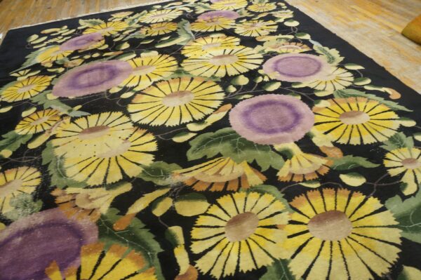 A black floral rug with large yellow and purple flowers lying on light wood planks.