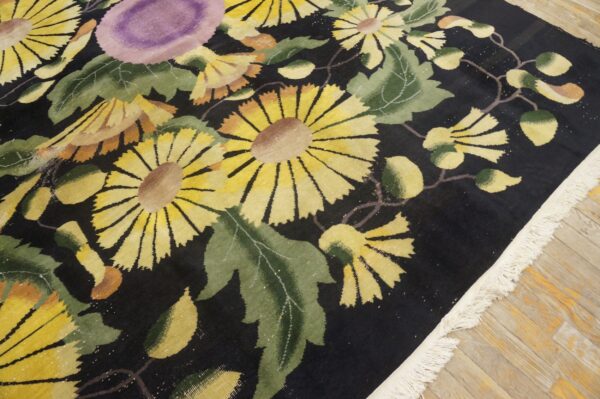 Black rug with bright yellow and purple flowers, green leaves, and white fringe detail on hardwood.