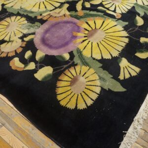 Close-up of a black, yellow, and purple high-pile floral rug on aged hardwood floorboards.