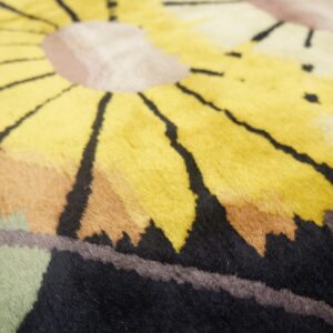Textured rug detail showing large yellow, black, brown, and green petals of a bold floral pattern.