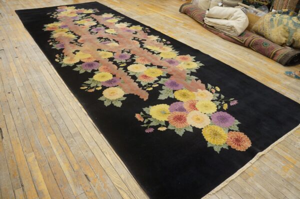 Long black rug with large pink, purple, and yellow floral designs rests on light wood planks.