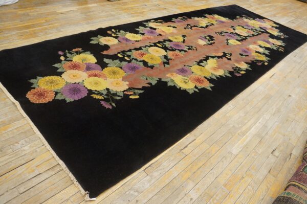 A long black rug features a vibrant floral pattern of yellow, purple, and orange flowers on wood plank floor.