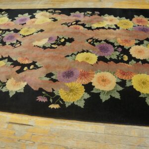 Plush black rug displaying colorful flowers and abstract pink stripes, resting on distressed blonde wood planks.