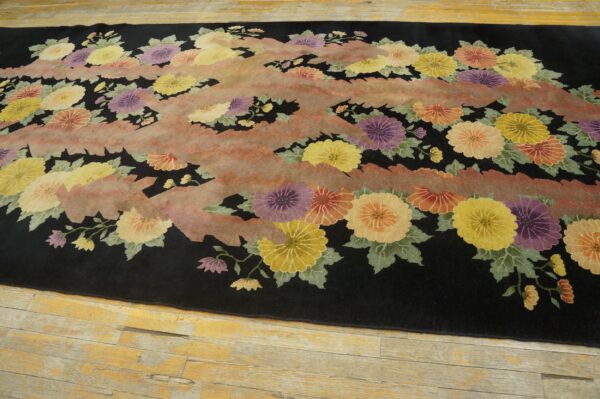 Plush black rug displaying colorful flowers and abstract pink stripes, resting on distressed blonde wood planks.