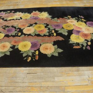 Black area rug with yellow, purple, and orange floral patterns and a central pink wavy band on distressed wood.