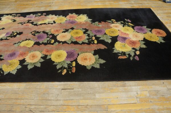 Black area rug with yellow, purple, and orange floral patterns and a central pink wavy band on distressed wood.
