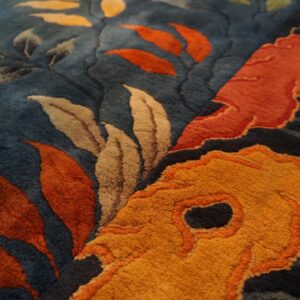 Sculpted pile details of a dark blue rug showing large orange, gold, and taupe floral and leaf patterns.