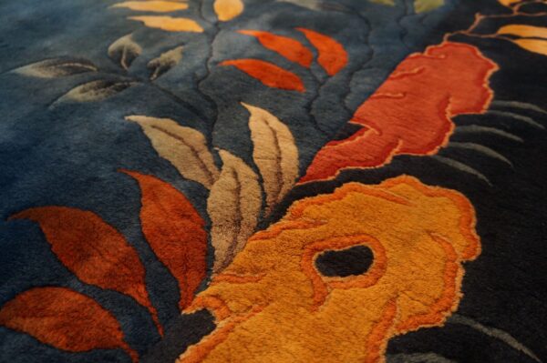 Sculpted pile details of a dark blue rug showing large orange, gold, and taupe floral and leaf patterns.