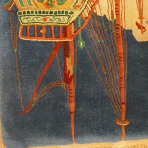 Detail of a deep blue rug displaying stylized orange, green, and tan decorative elements on wood flooring.