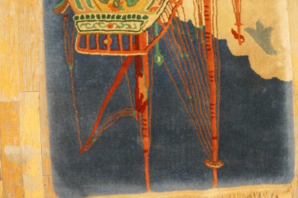 Detail of a deep blue rug displaying stylized orange, green, and tan decorative elements on wood flooring.