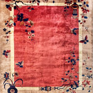 Red field rug with a tan border decorated with blue and red flowers, vines, and ornate vases.