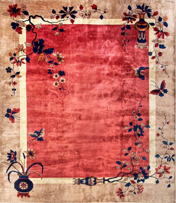 Red field rug with a tan border decorated with blue and red flowers, vines, and ornate vases.