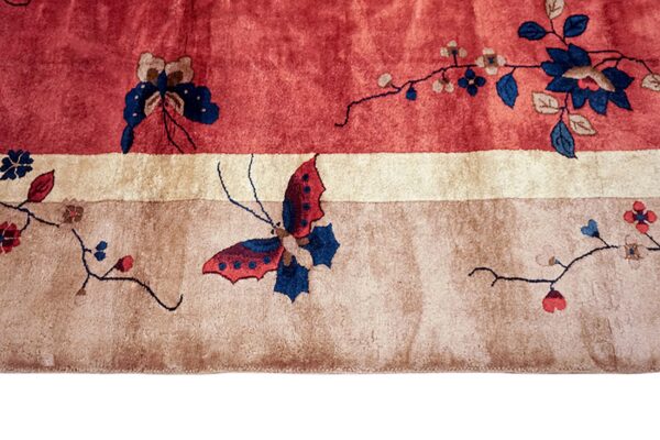 A close-up of a rug featuring red, ivory, and taupe bands with floral and butterfly patterns.