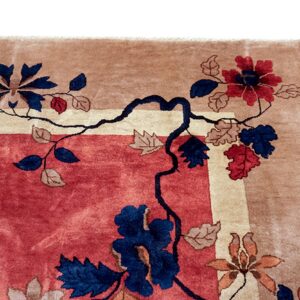Corner of a deep pile rug with a rose field, tan border, and navy blue and red floral patterns.