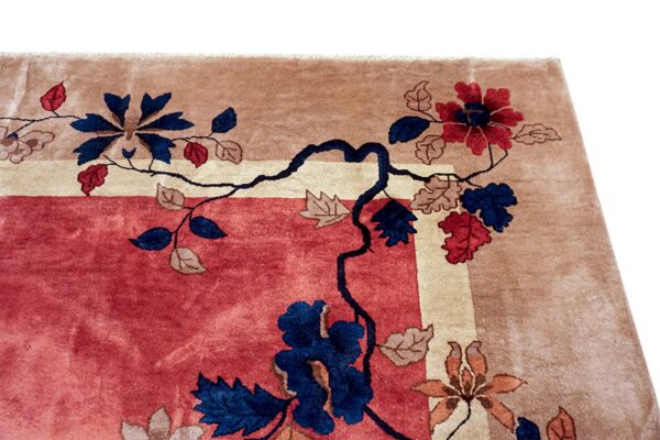 Corner of a deep pile rug with a rose field, tan border, and navy blue and red floral patterns.