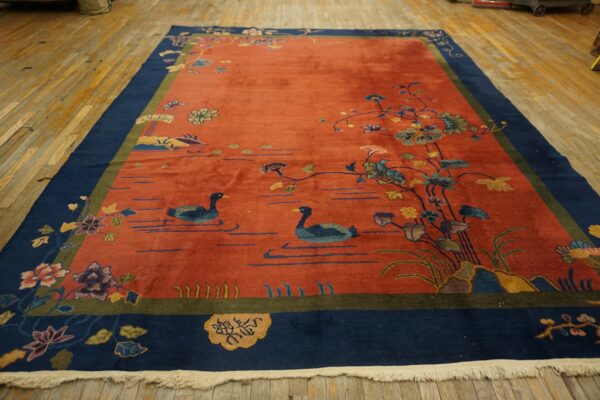A low-pile, rust and blue scenic rug showing ducks and flowers, laid upon distressed wooden planks.