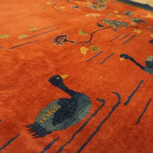 Rust-toned rug with deep pile features a pictorial pattern of blue geese, vines, and scattered florals.